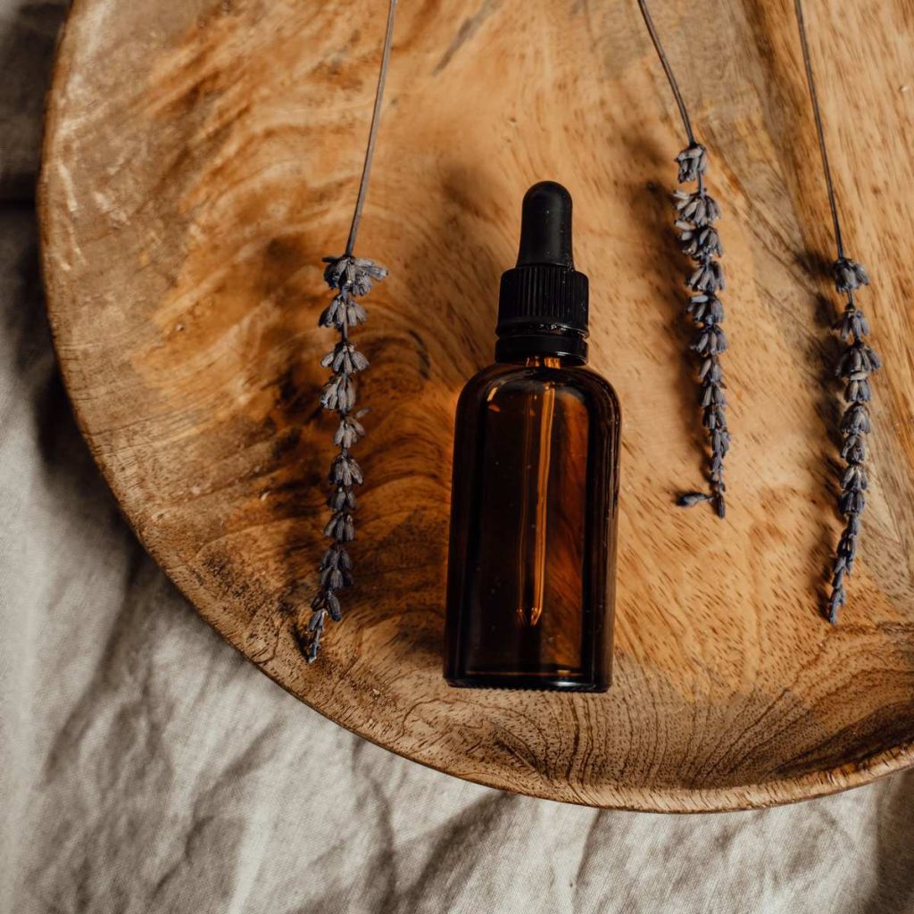 Amber glass dropper bottle with dried lavender sprigs on a round wooden dish